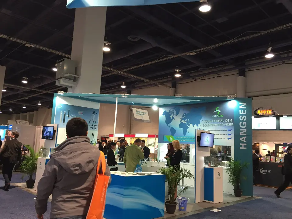 Visitors walking past the teal and white HANGSEN booth with plants and screens