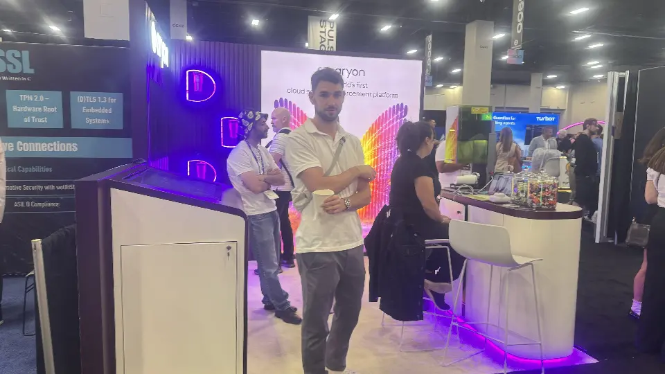 Two people stand at the Aryon booth in front of purple lit arcs and the slat wall
