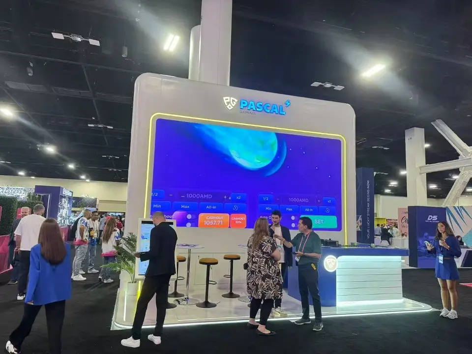 Pascal Gaming booth with a large screen, white stools and visitors in front