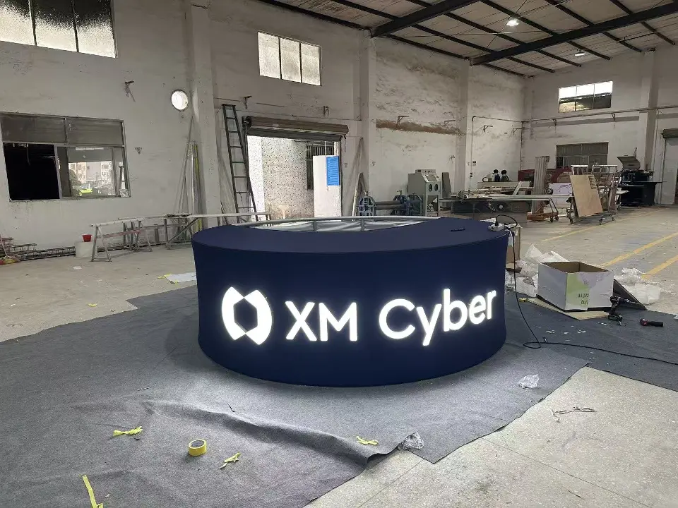 Round dark counter with backlit XM Cyber logo on a workshop floor