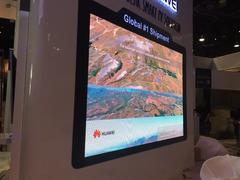 Large video screen in a white column showing an aerial view of terraced hills