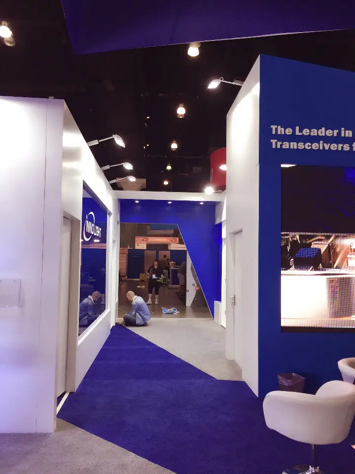 Corner of the booth with blue carpet and The Leader in High Speed Optical graphic