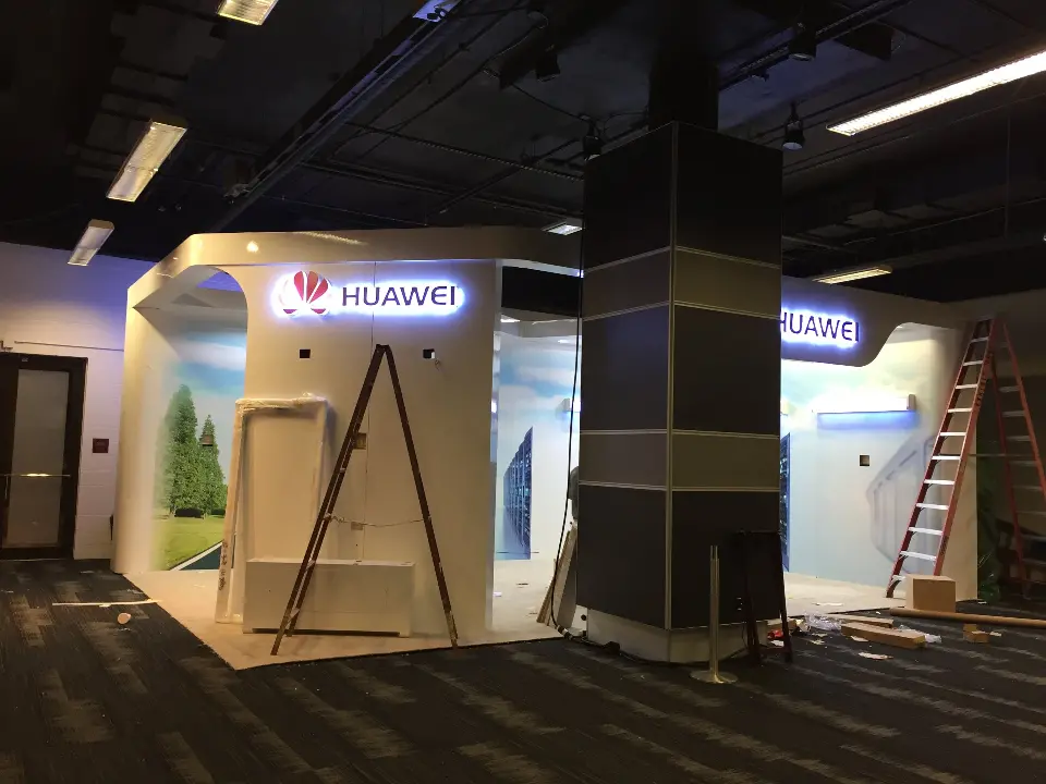During installation: Huawei booth front with a ladder by the lit logo and wrapped column