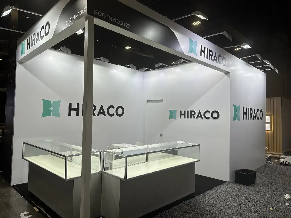 Angled view of the HIRACO booth with lit glass counters and teal branding
