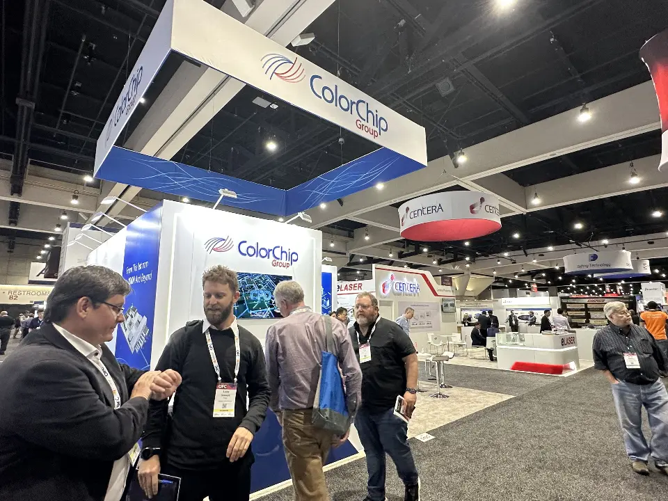 Visitors talking at the front edge of the booth beneath the angled sign
