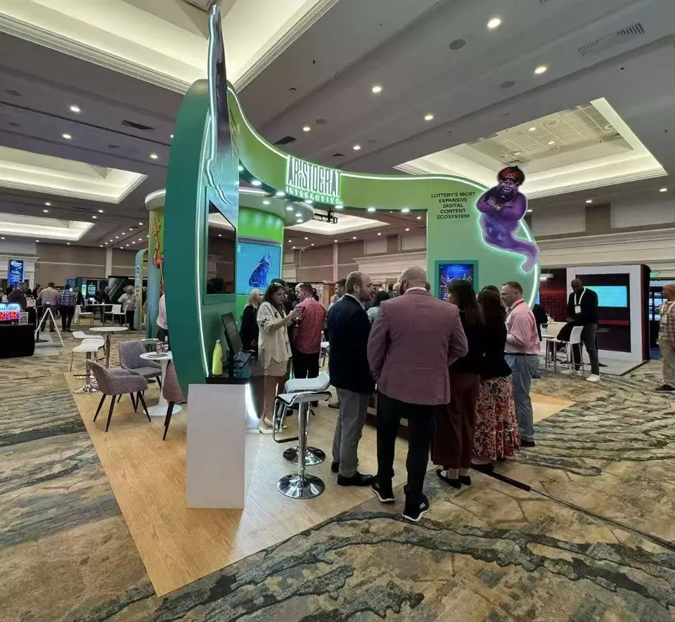 Visitors gathered under the Aristocrat Interactive arch beside a green curved wall and a genie cut-out