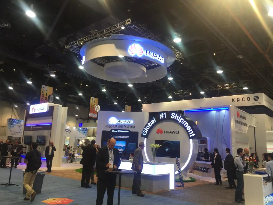 Wide show-floor shot of the booth front with people near the screens