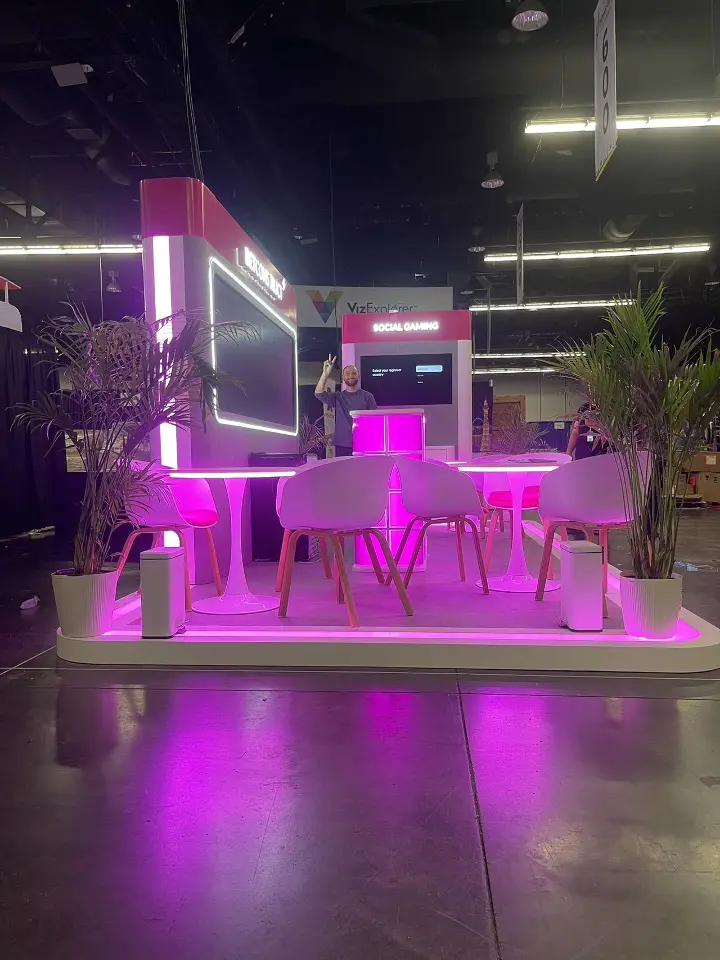 Front of the booth with white chairs, palm plants and lit platform edge
