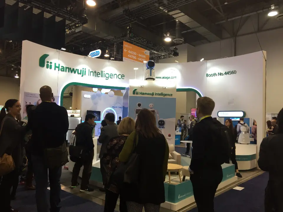 Visitors watching robot demos along the front of the white and teal booth