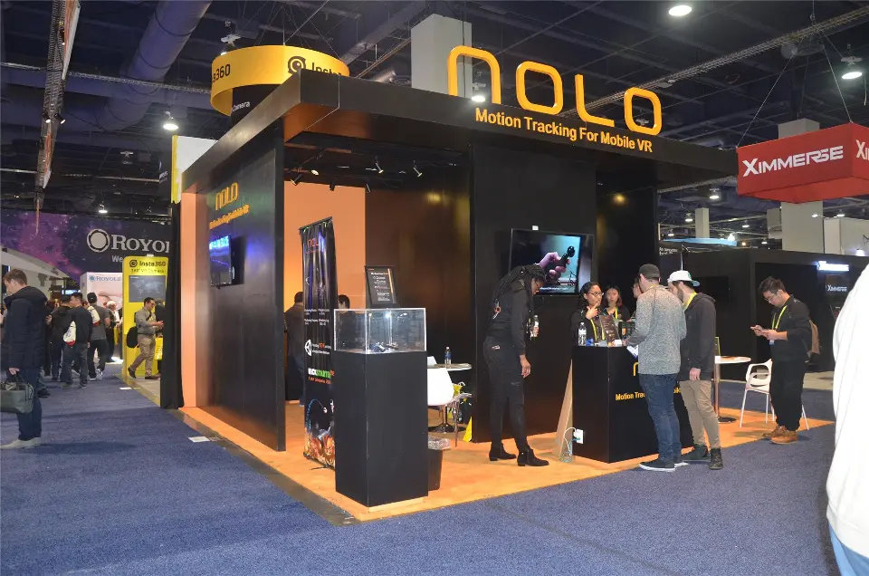 Wide aisle view of the NOLO booth with glass pedestals and visitors