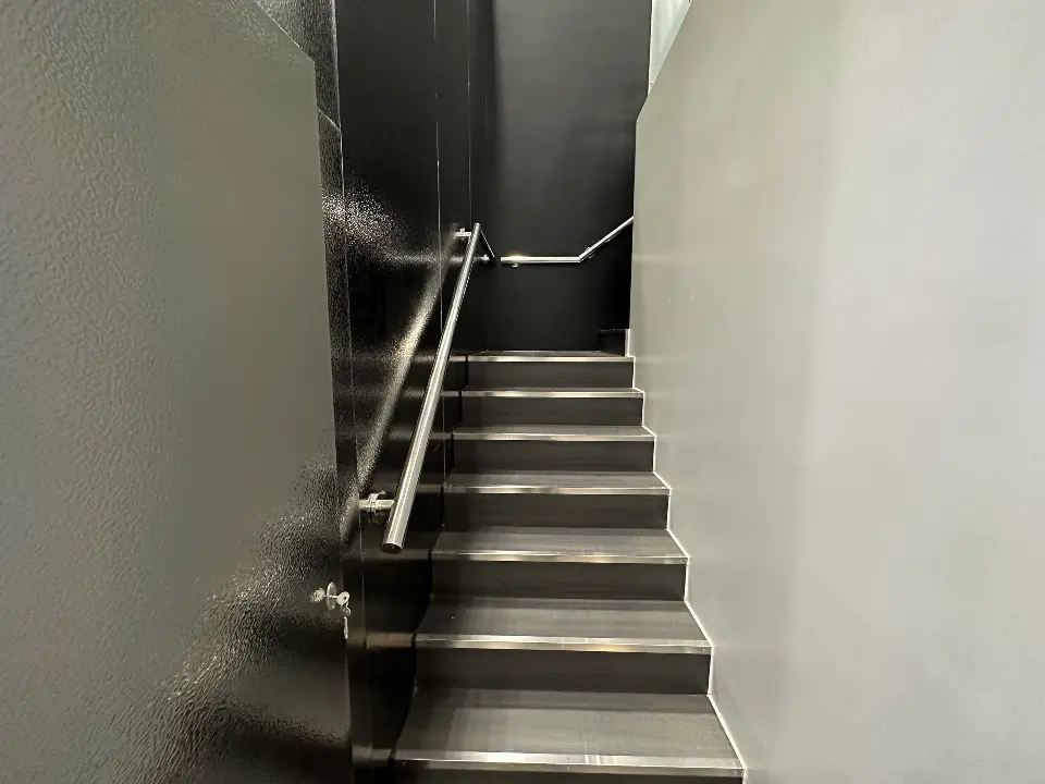 Black staircase with handrail beside a white wall