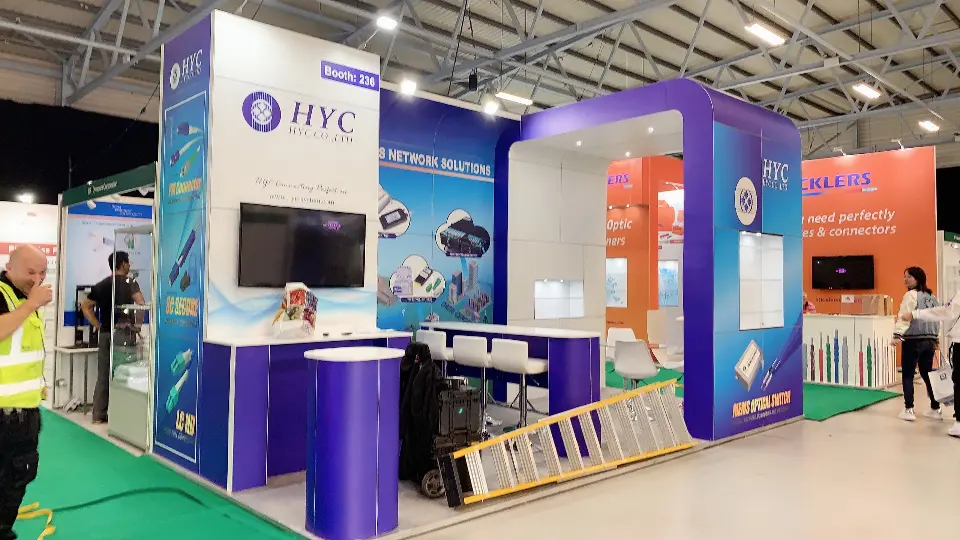 During build-up: HYC purple and white booth with round counter, wall screen and ladder