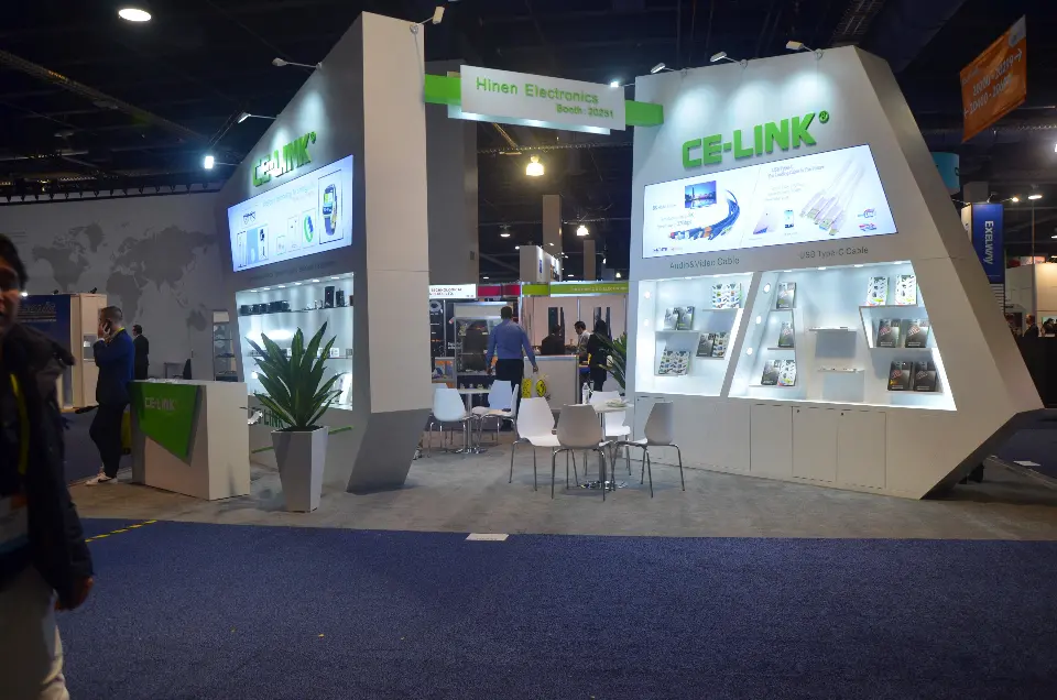 Aisle view of CE-LINK walls with backlit cable graphics, lit shelves and white meeting chairs