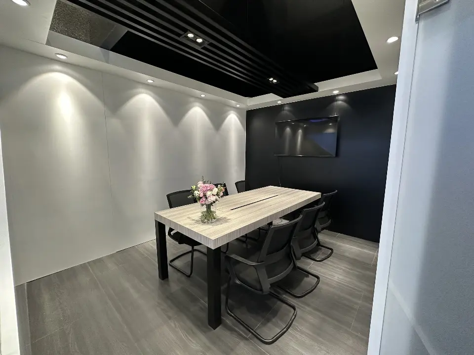 Meeting room with white table, black chairs and a dark wall screen