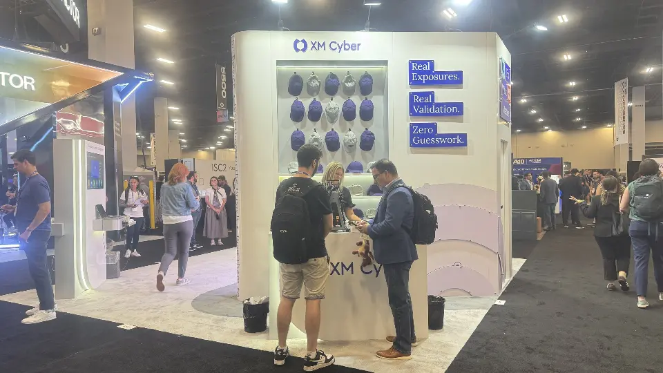 Visitors at the XM Cyber display wall with navy shapes and blue headline panels