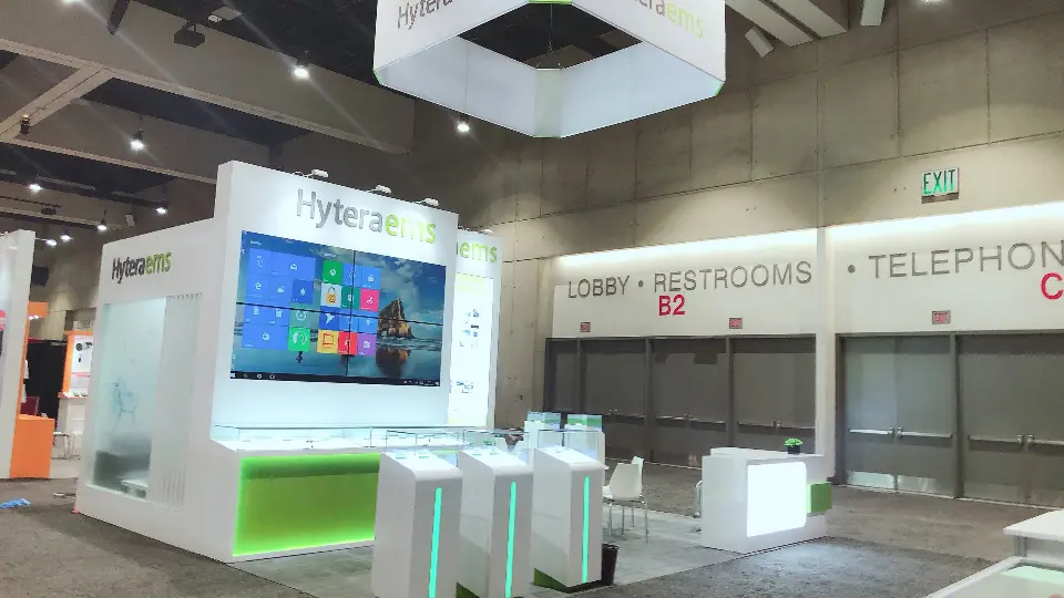 Finished Hyteraems booth with tiled video wall, glass showcases and green-lit counter