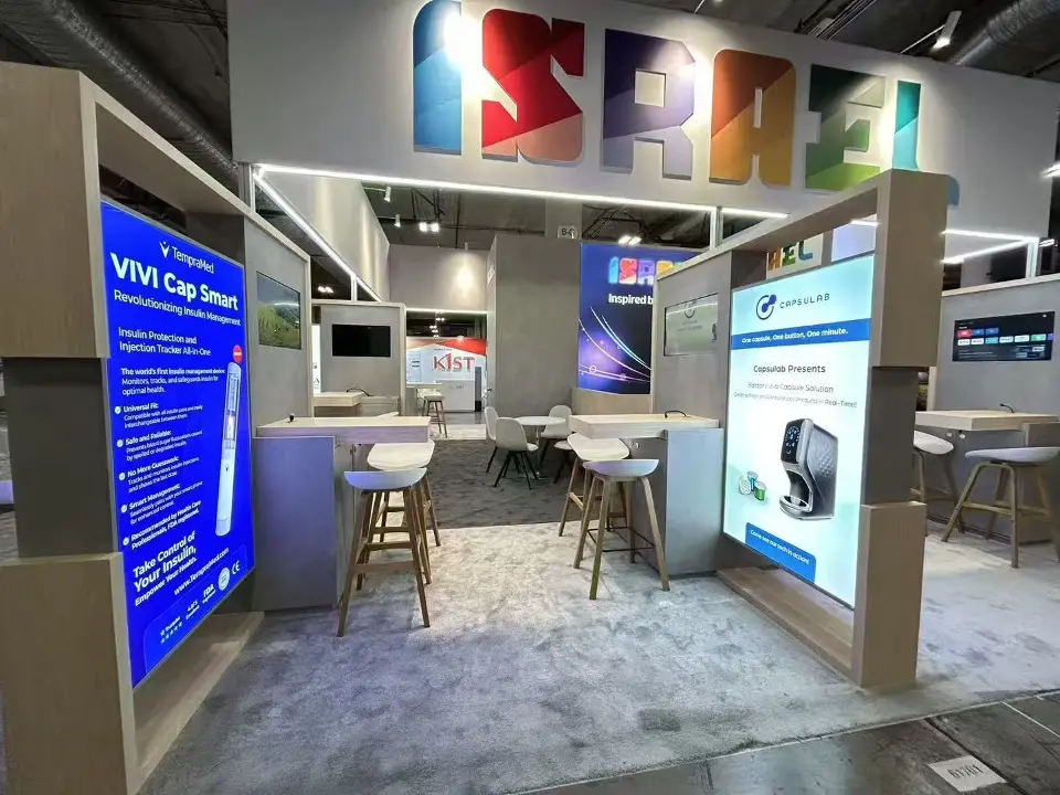 Aisle inside the Israel Pavilion at CES 2025 lined with lightbox exhibitor pods and high tables