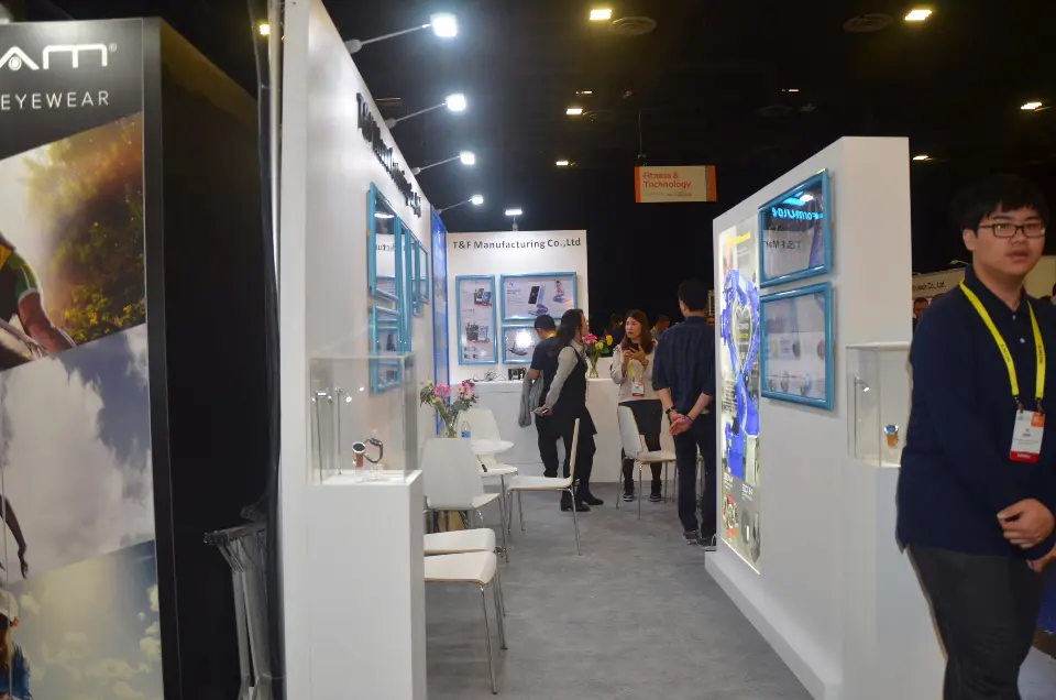 Aisle view along white T&F Manufacturing walls with backlit product panels and a visitor