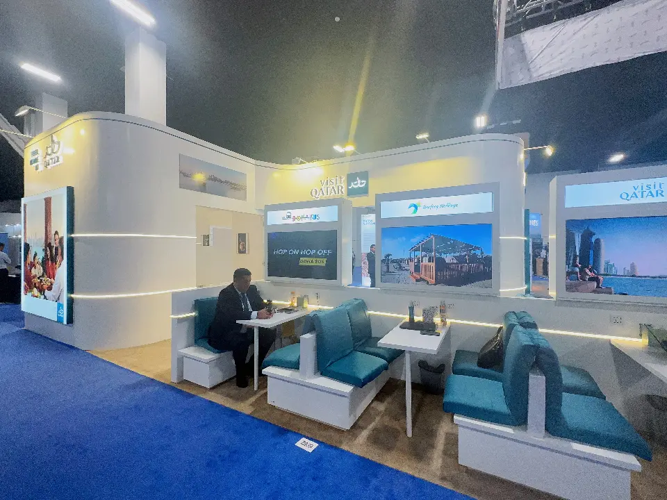 Teal upholstered booth seating with small tables and partner screens inside the Qatar pavilion