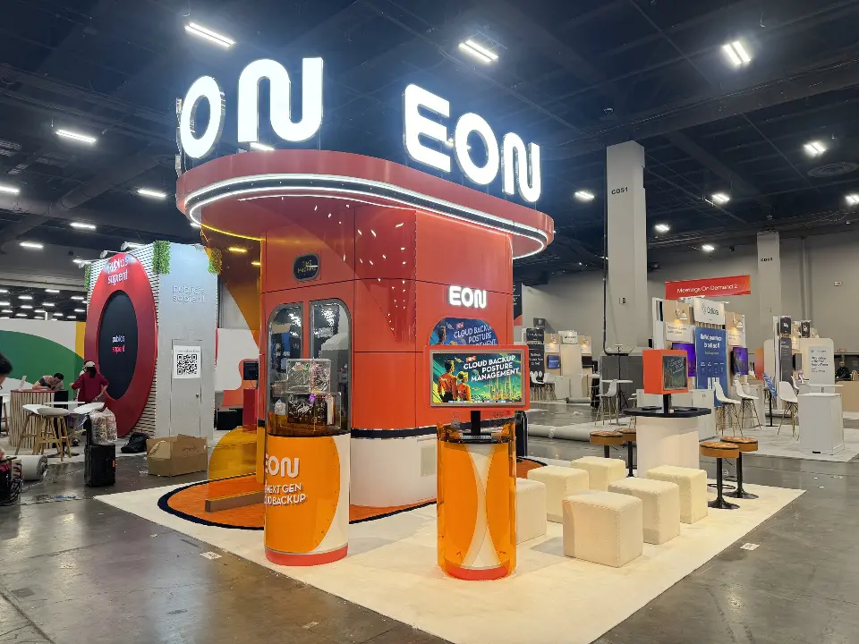 EON booth with white letters above an orange curved tower and cube seating