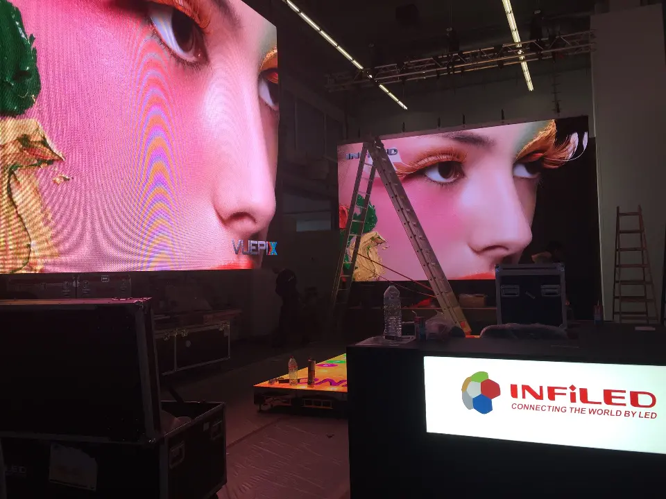 Large video screen showing a close-up face beside a white logo counter