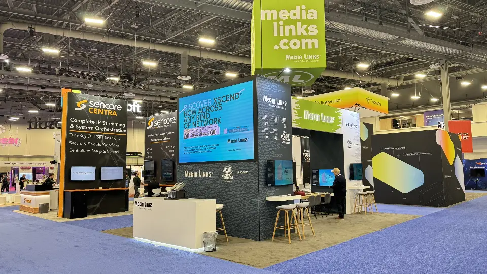 Finished Media Links stand on blue carpet with screens, counter and green banner