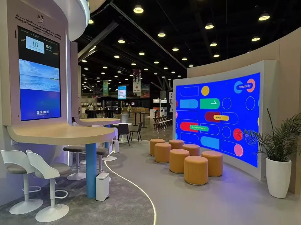 Counter seating with white stools facing a large colorful video screen and orange poufs