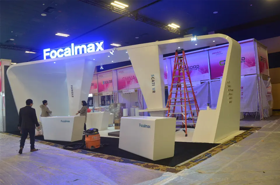 During build-up: Focalmax booth with angled white arch walls and blue lit logo, ladders in place