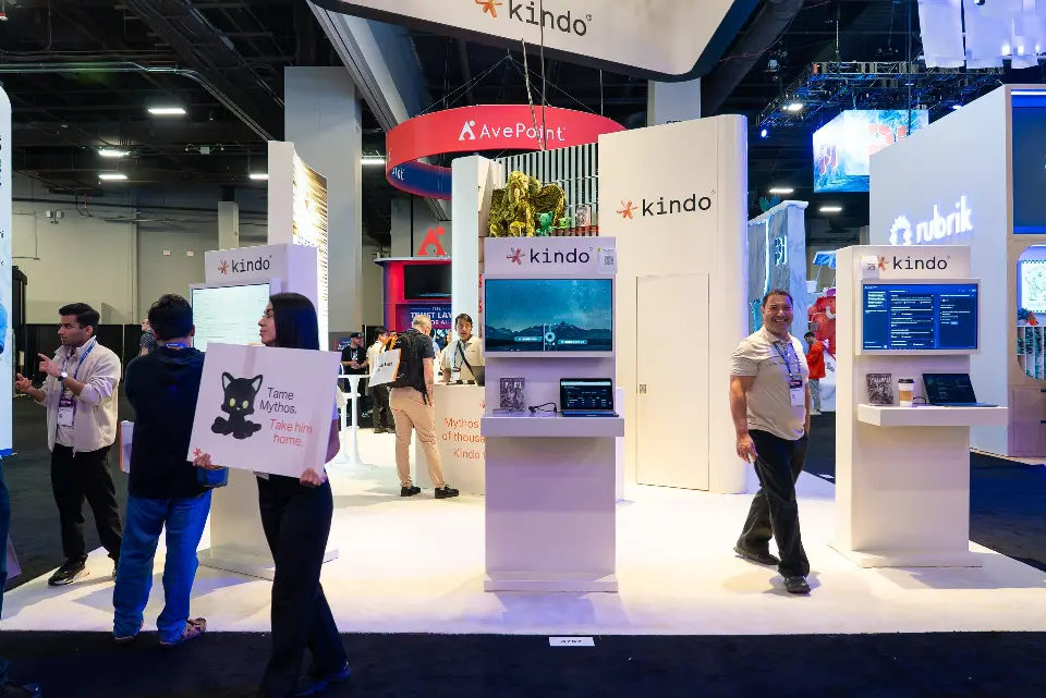 Open front of the white kindo booth with screen kiosks and visitors in the aisle