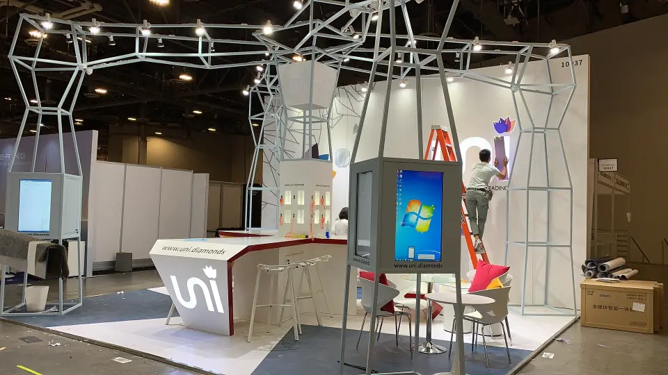 uni booth with wire-frame diamond outline overhead, white counter and screen kiosks