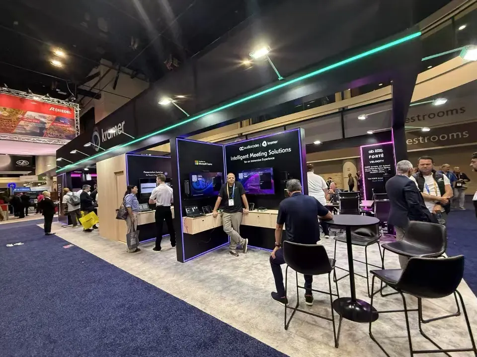 Aisle view with teal light strip, demo screens and visitors at tables