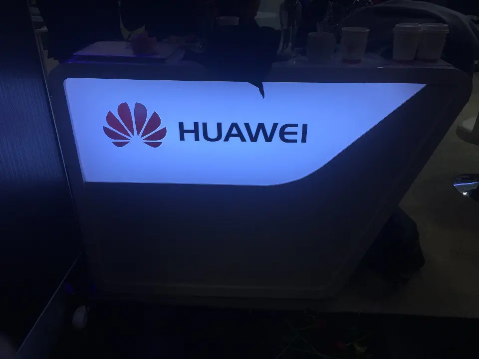 Close view of a backlit Huawei logo panel on a dark angled wall