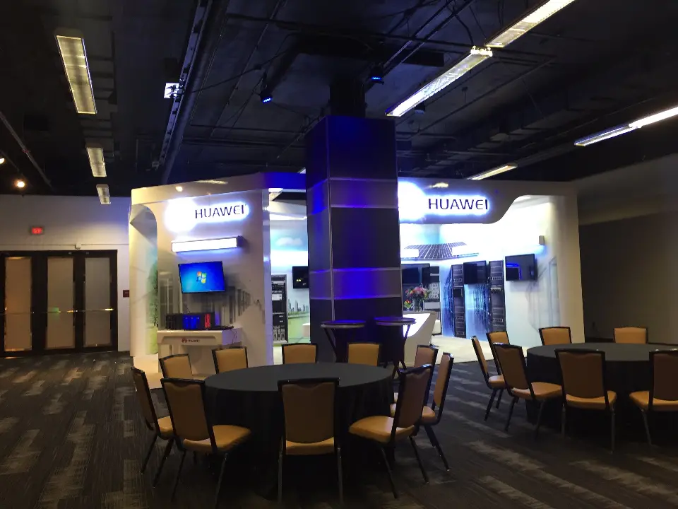 Huawei booth seen across round tables with the blue-lit column and server displays