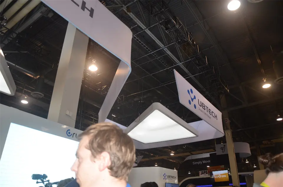 Angled UBTECH hanging sign and lit ceiling panel above the white booth