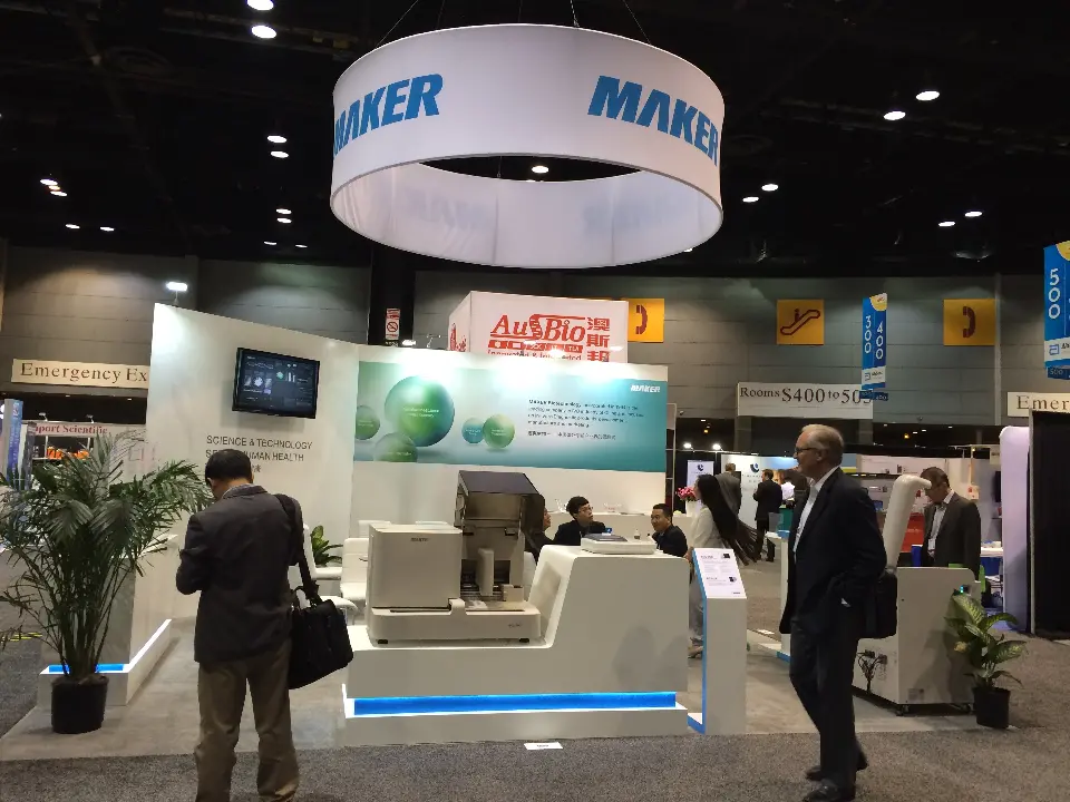 Front view of the MAKER stand with green sphere graphic wall, wall screen and blue-lit instrument plinths