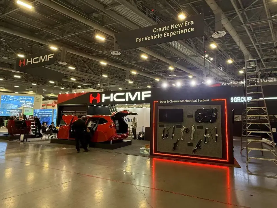 Rear view of a lit product display wall beside a red vehicle and the HCMF sign