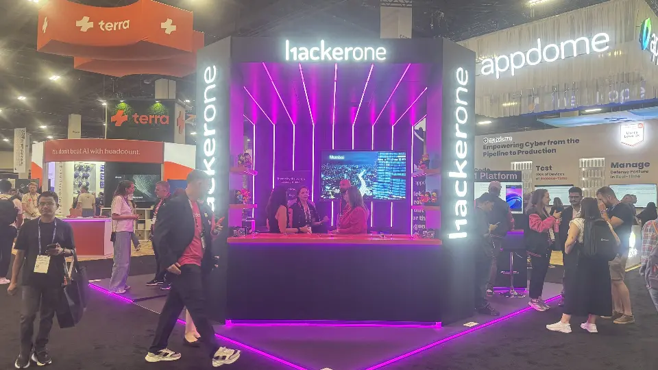Busy aisle view of the black hackerone booth with magenta light lines