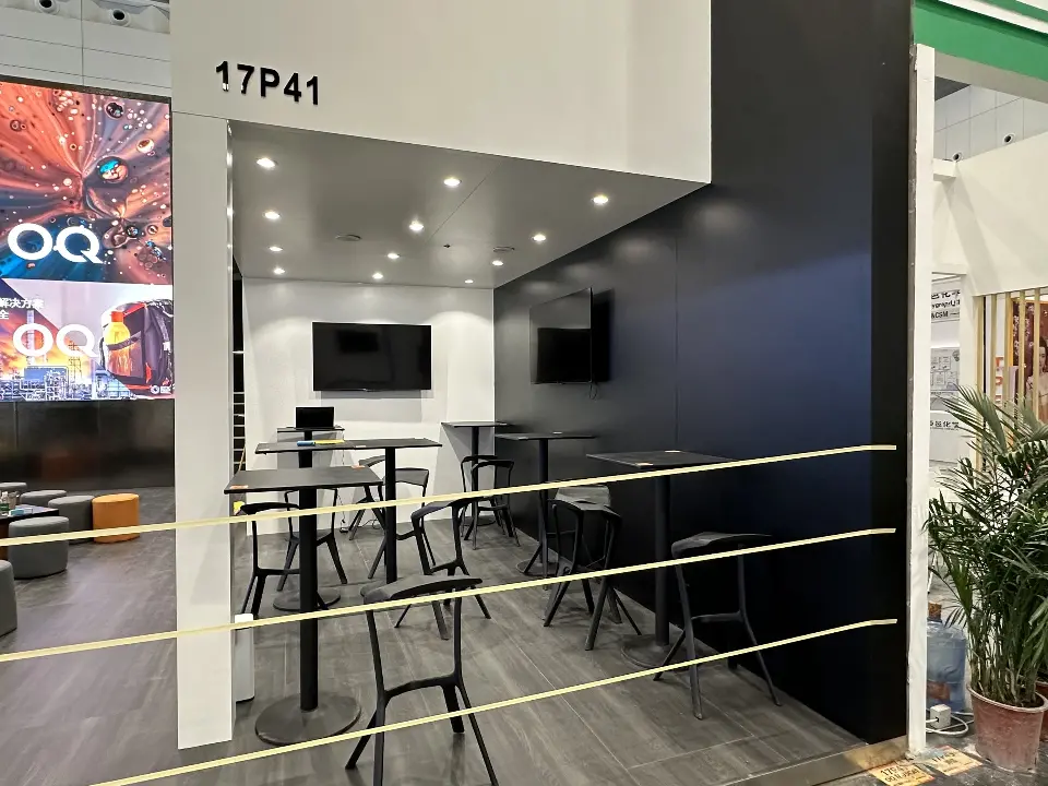 Open booth corner with bar tables, a wall screen and the black wall