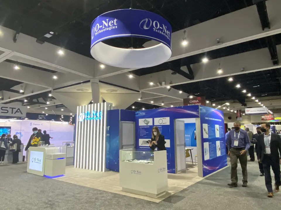 Aisle view of the O-Net booth with visitors, white counters and the blue ring sign
