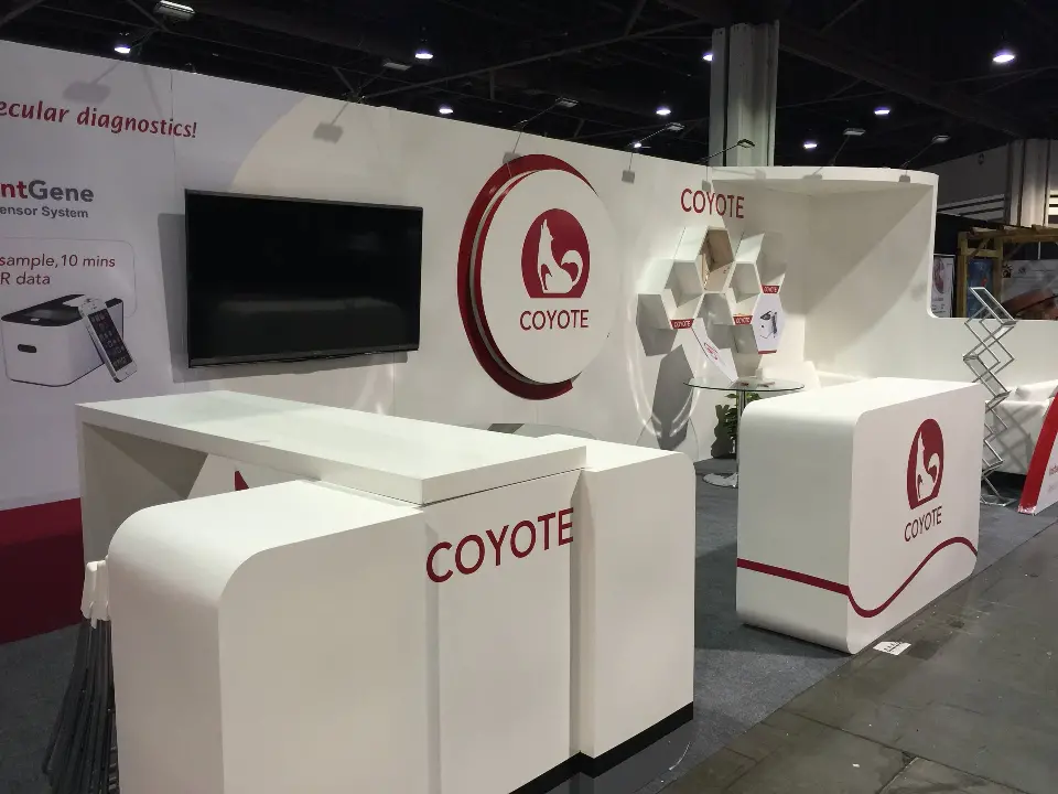 COYOTE-branded white counters in front of the red logo wall and wall screen