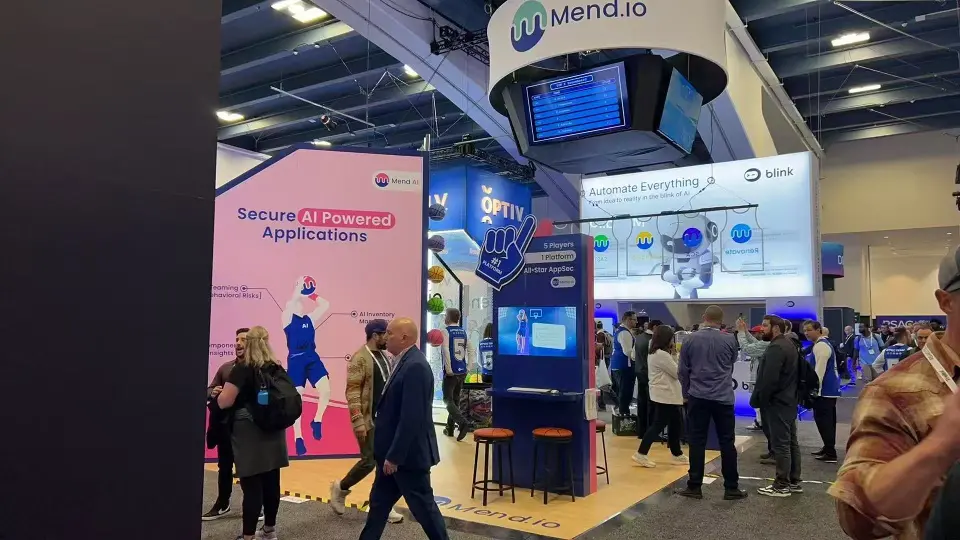 Visitors passing the pink Secure AI Powered Applications wall and stools under the Mend.io drum sign