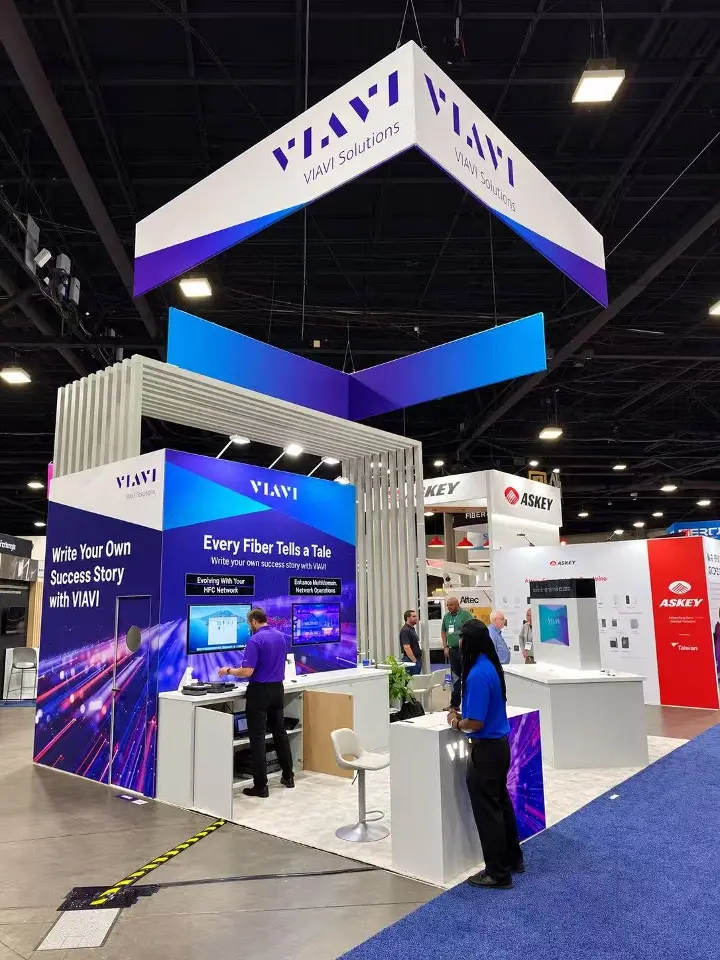 VIAVI Solutions booth seen from the aisle, with staff at white counters under a slatted white canopy