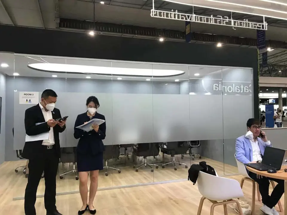 Staff greeting guests near a wood-floor seating area with white chairs
