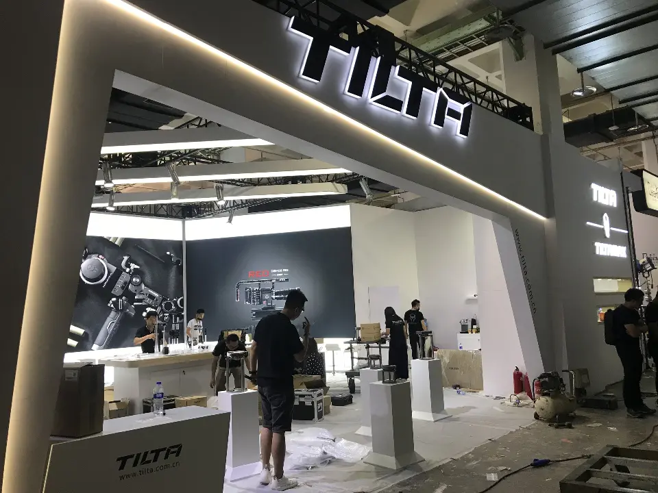 During build-up: dark booth with TILTA sign, angled light strips and display plinths being placed