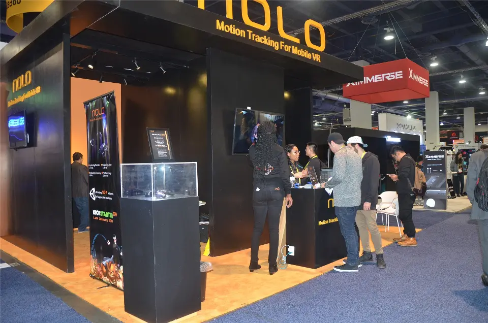 Side view of the NOLO stand with glass product case, roll-up banner and visitors at the counter