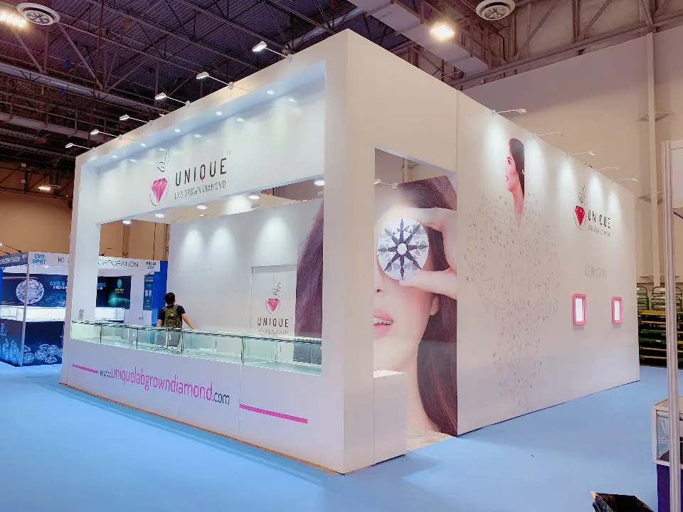 White booth with a pink UNIQUE logo, a model face graphic and glass showcases