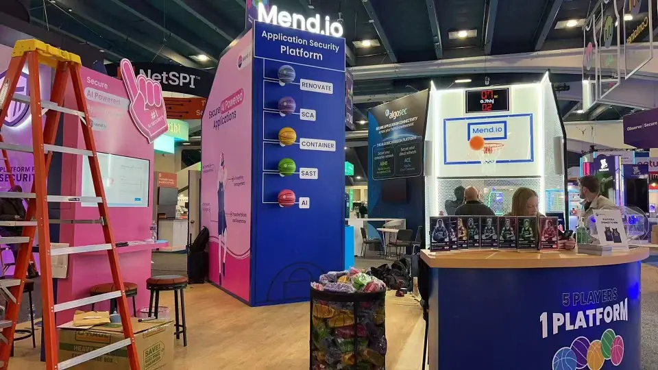 Mend.io counter with 1 Platform branding and pink graphic wall, ladder still nearby