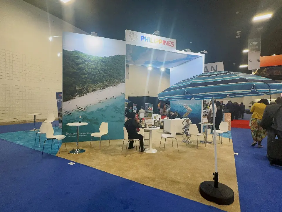 Beach-scene backdrop with white tables, chairs and a blue umbrella on the stand