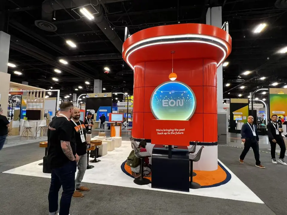 Rear of the red EON kiosk with a round illuminated logo display and a small seating table