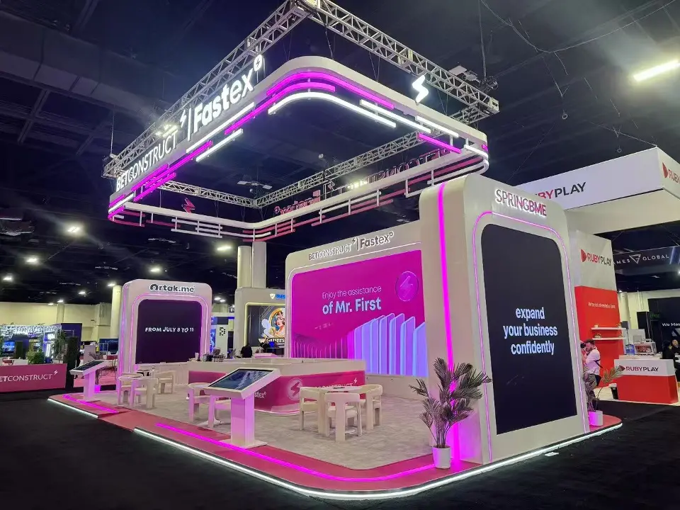 Angled view of pink screen walls, white seating and touch-screen tables